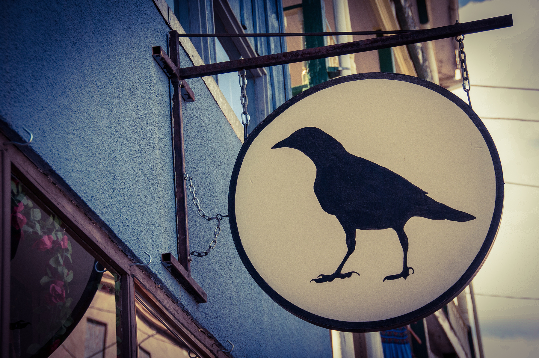 Auto-generated description: A black silhouette of a bird is depicted on a round, hanging sign outside a building.