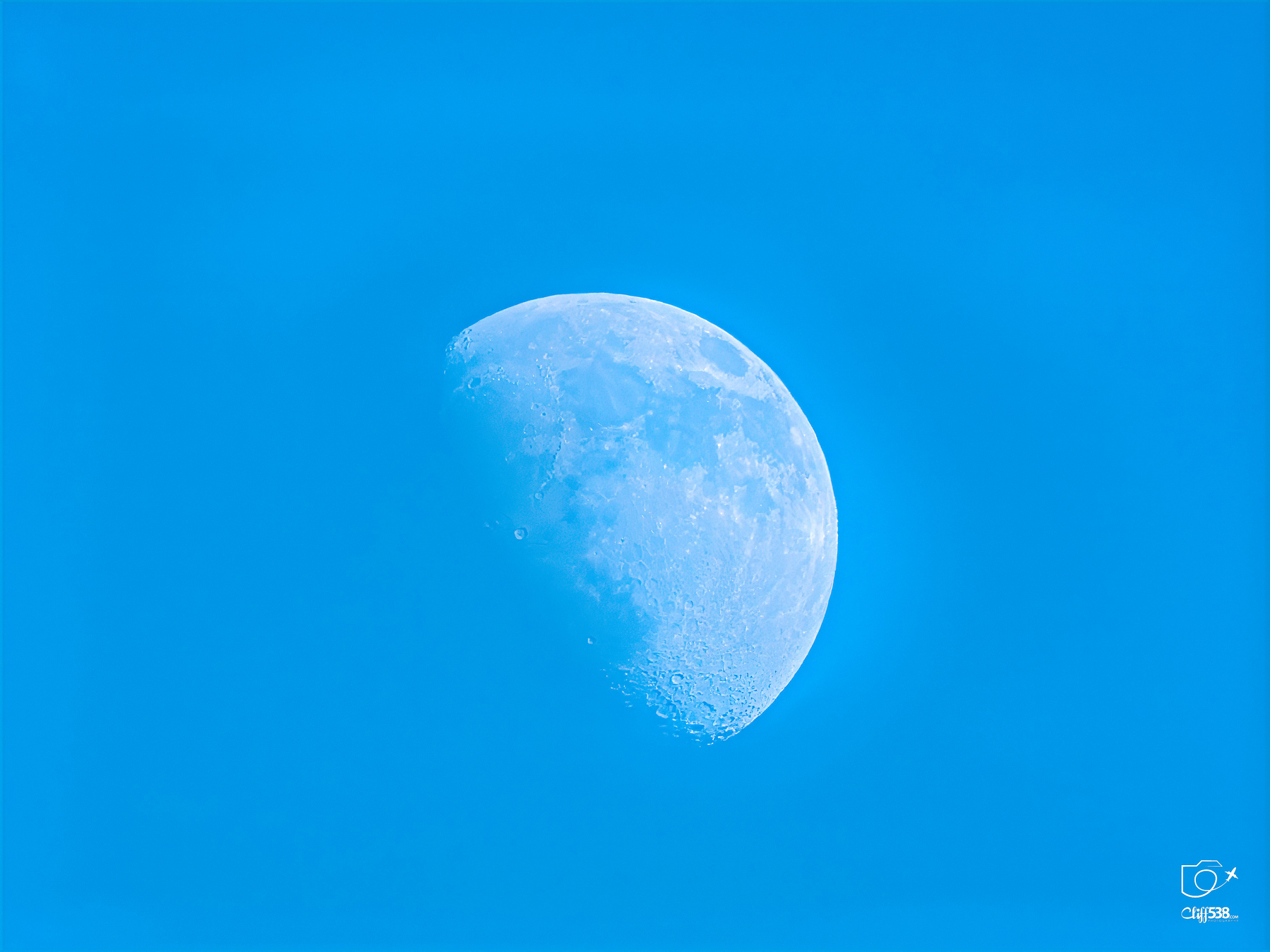Auto-generated description: A bright half-moon appears vividly against a clear blue sky.