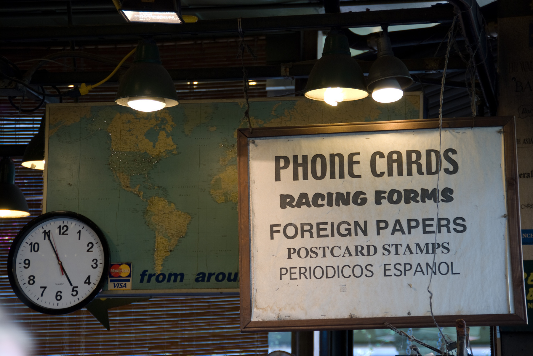 Auto-generated description: A clock and a sign listing various items for sale hang in front of a map of the world.