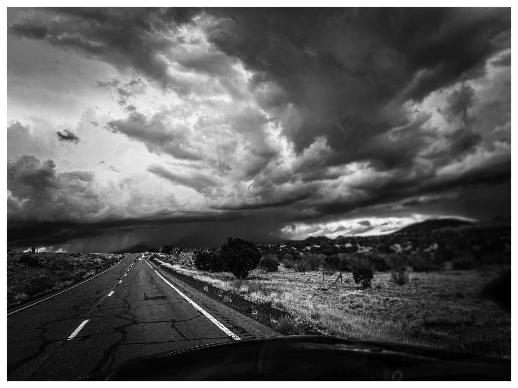 Auto-generated description: A dramatic, expansive sky filled with dark, swirling storm clouds looms over an empty rural road and sparse landscape.
