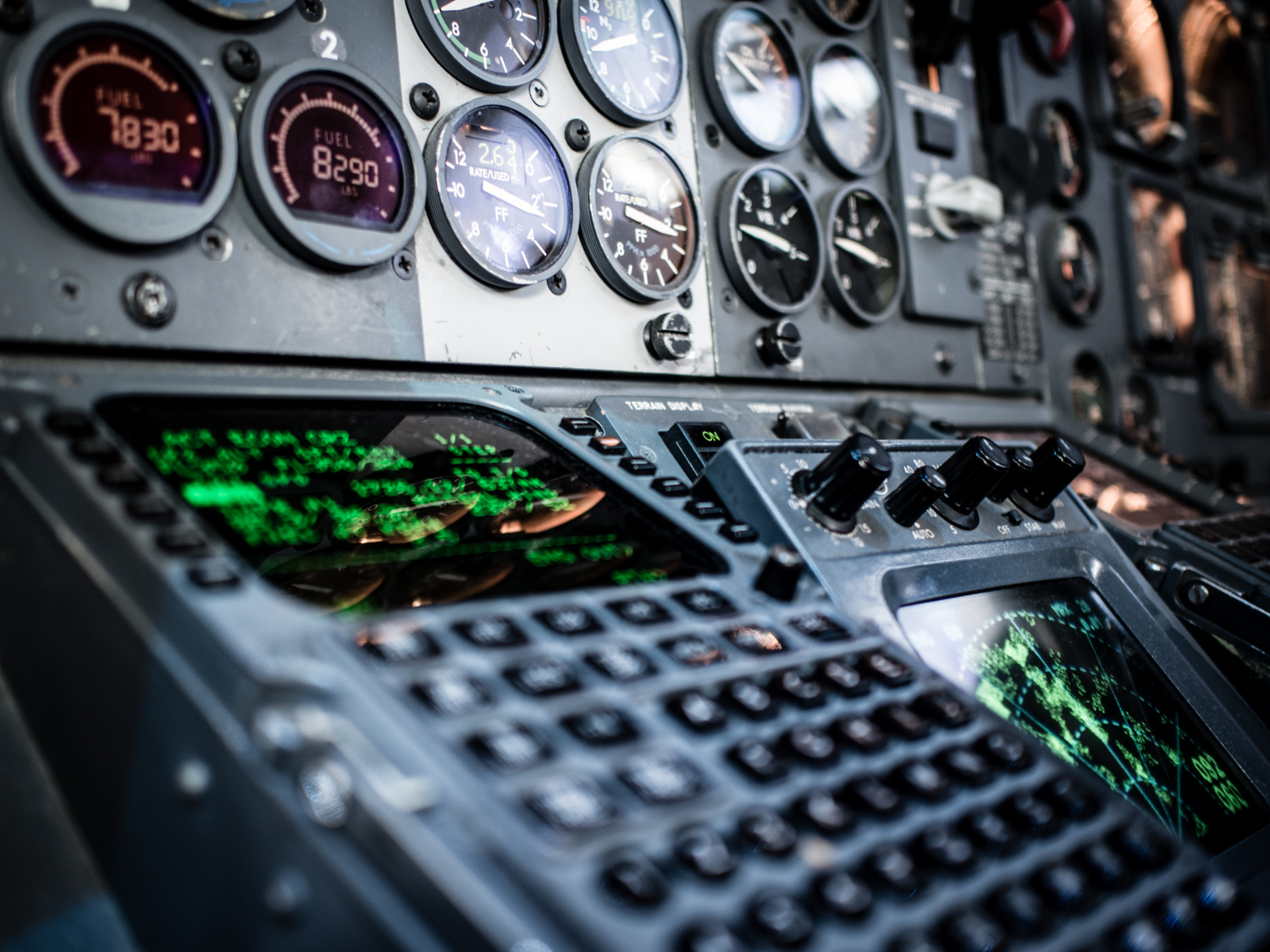Auto-generated description: A cockpit control panel with various gauges, screens, and buttons is illuminated with green displays.