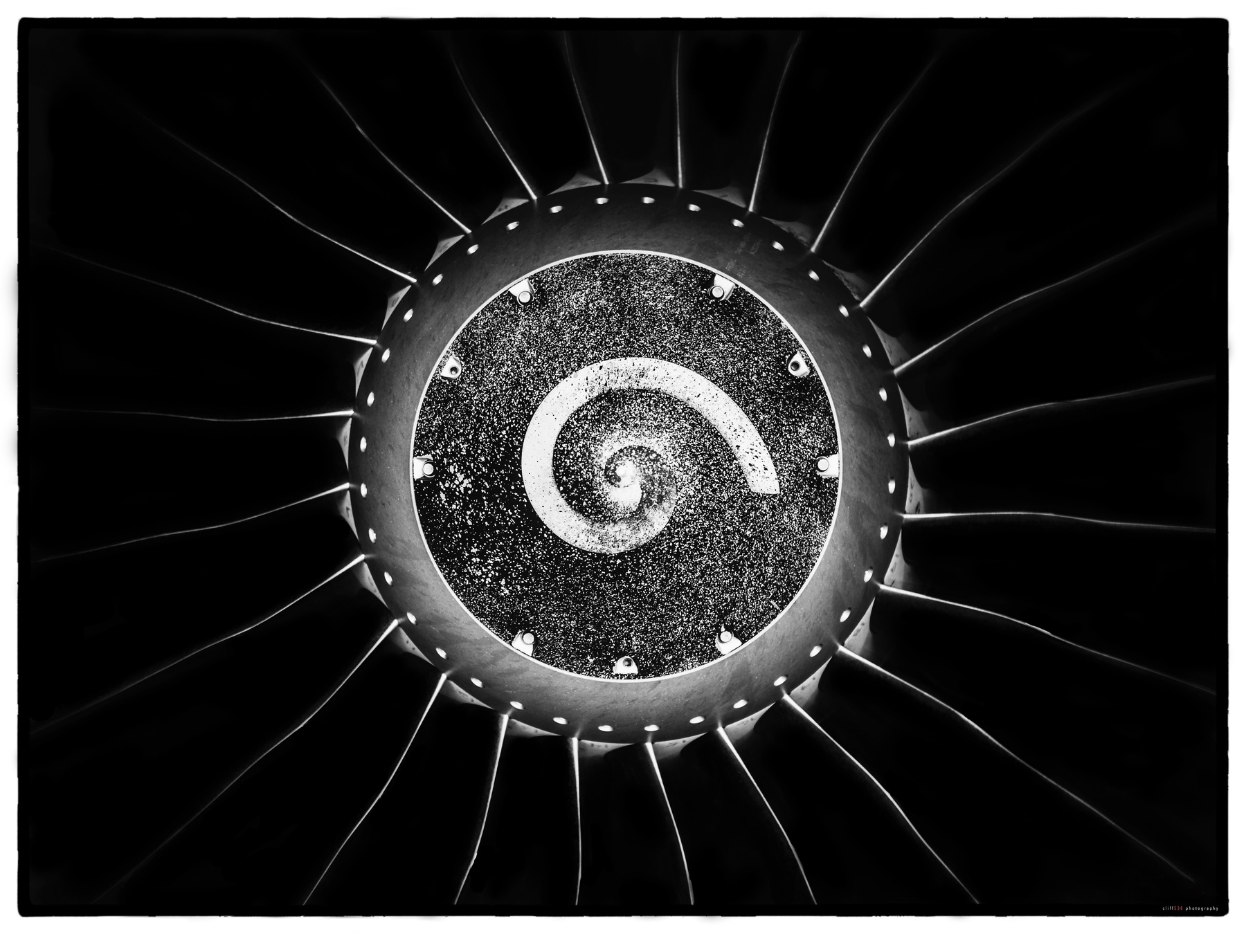 Auto-generated description: A circular abstract pattern resembling a spiral galaxy is surrounded by radiating lines and dots in black and white.