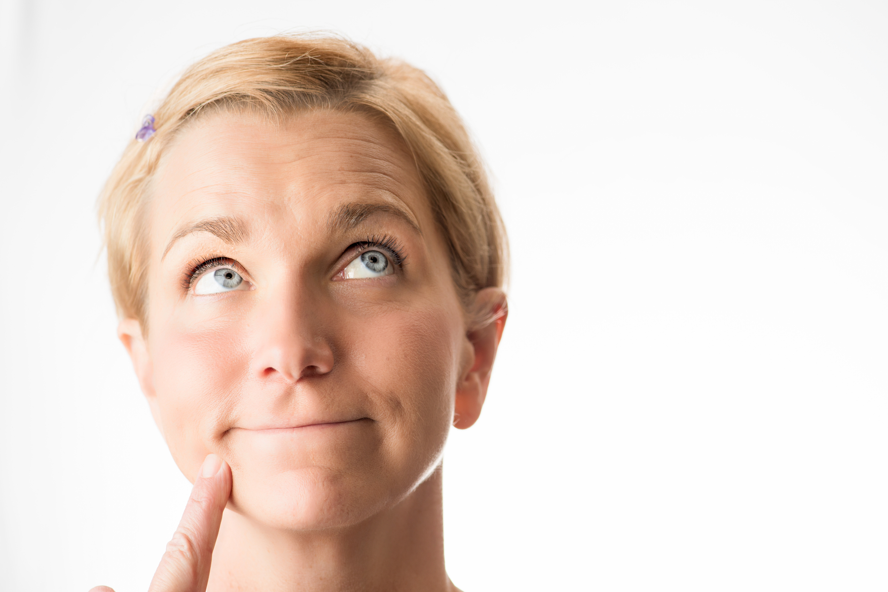 Auto-generated description: A person with short blonde hair is looking up thoughtfully with their finger on their chin.