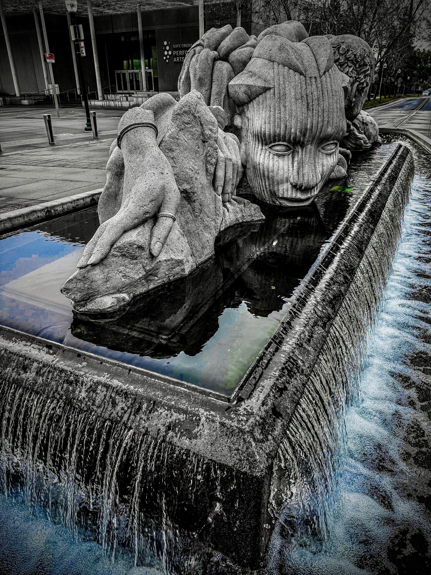 Auto-generated description: A large stone sculpture depicting a face and hands rests in a flowing water fountain.