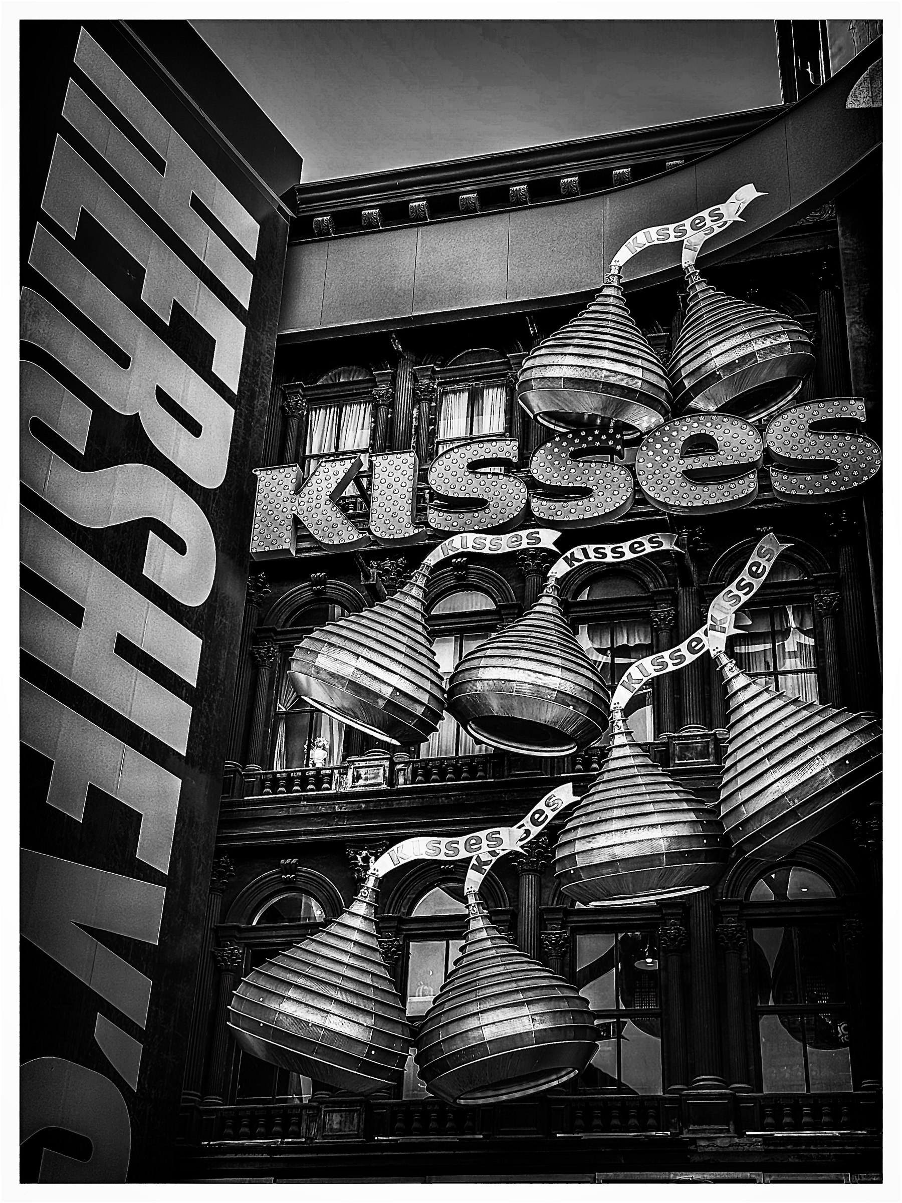 Auto-generated description: Large metallic Hershey's Kisses decorations hang in front of a building, accompanied by a prominent HERSHEY'S sign.