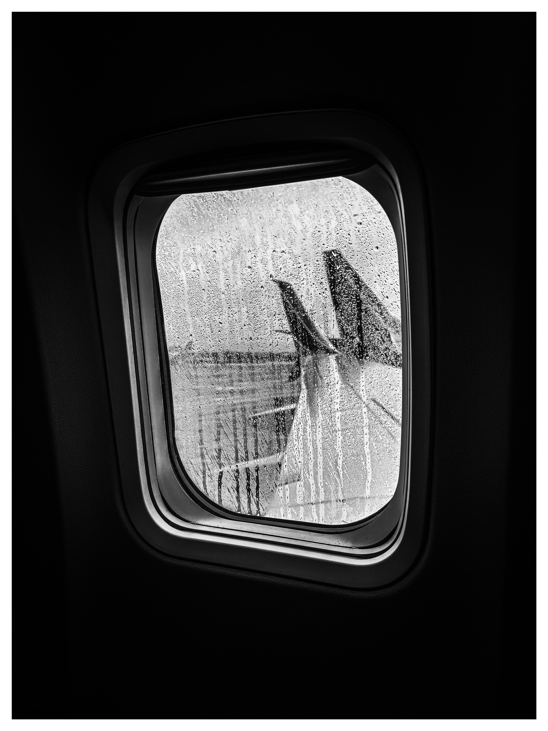 Auto-generated description: Raindrops streak down an airplane window with the aircraft's wing visible in the background.