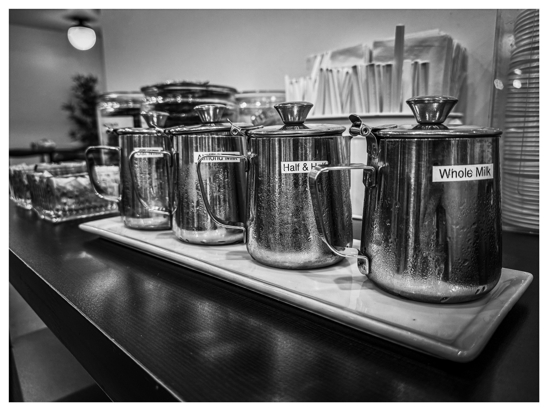 Auto-generated description: A row of metal containers labeled Non-Dairy, Half & Half, and Whole Milk sits on a tray alongside cups and straws.