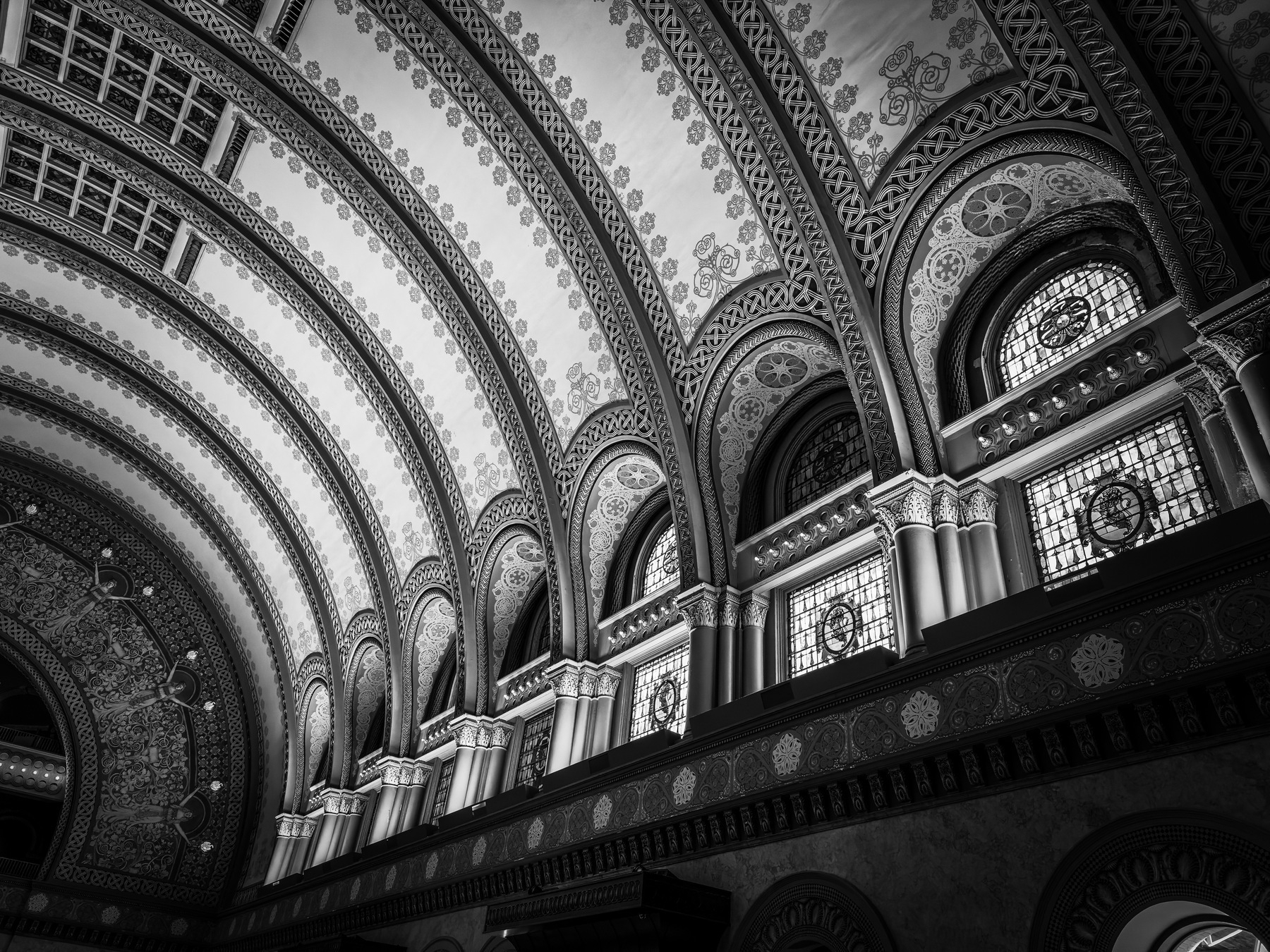 Auto-generated description: A series of intricately designed stained glass windows and ornately decorated arches are featured in an architecture with a black-and-white theme.