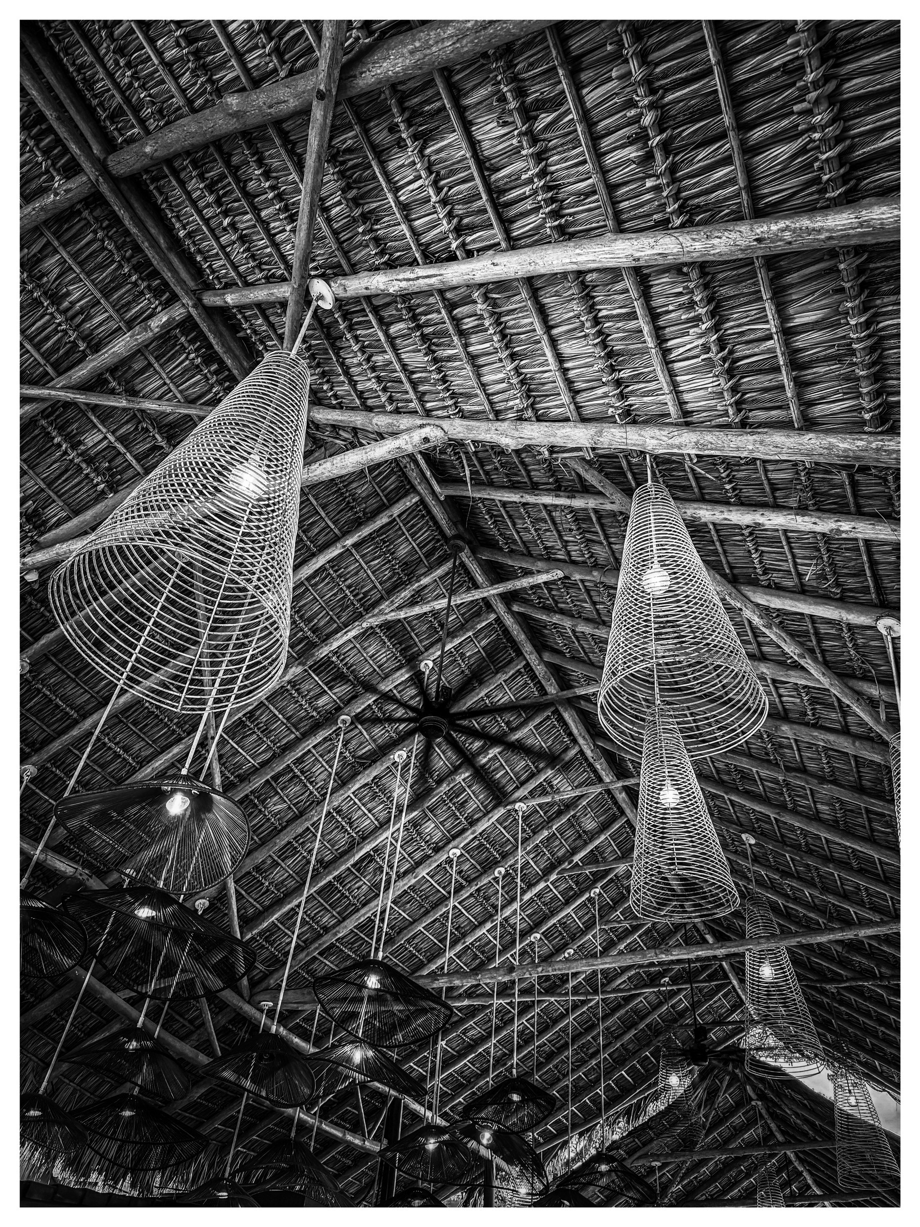 Auto-generated description: A thatched roof interior features modern, cone-shaped wire lights and a large ceiling fan.