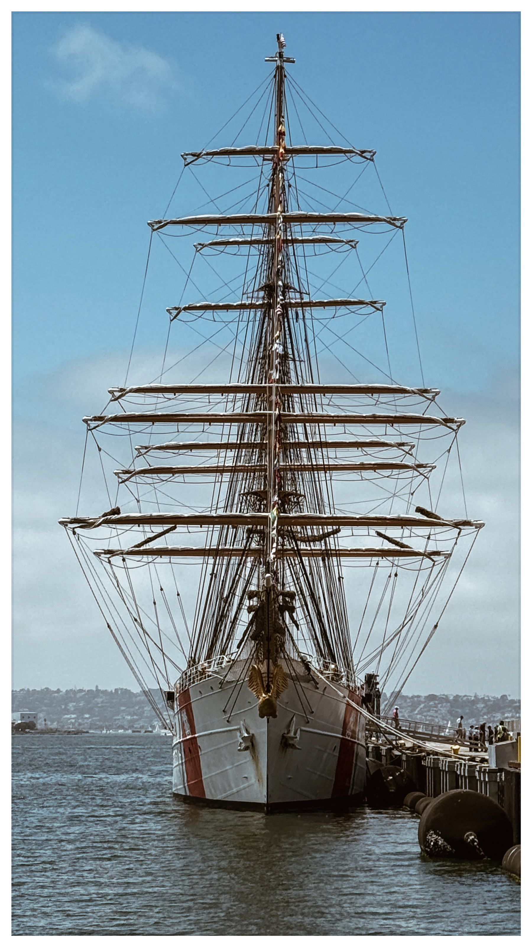 Auto-generated description: A large, multi-masted sailing ship is docked at a pier under a clear blue sky.