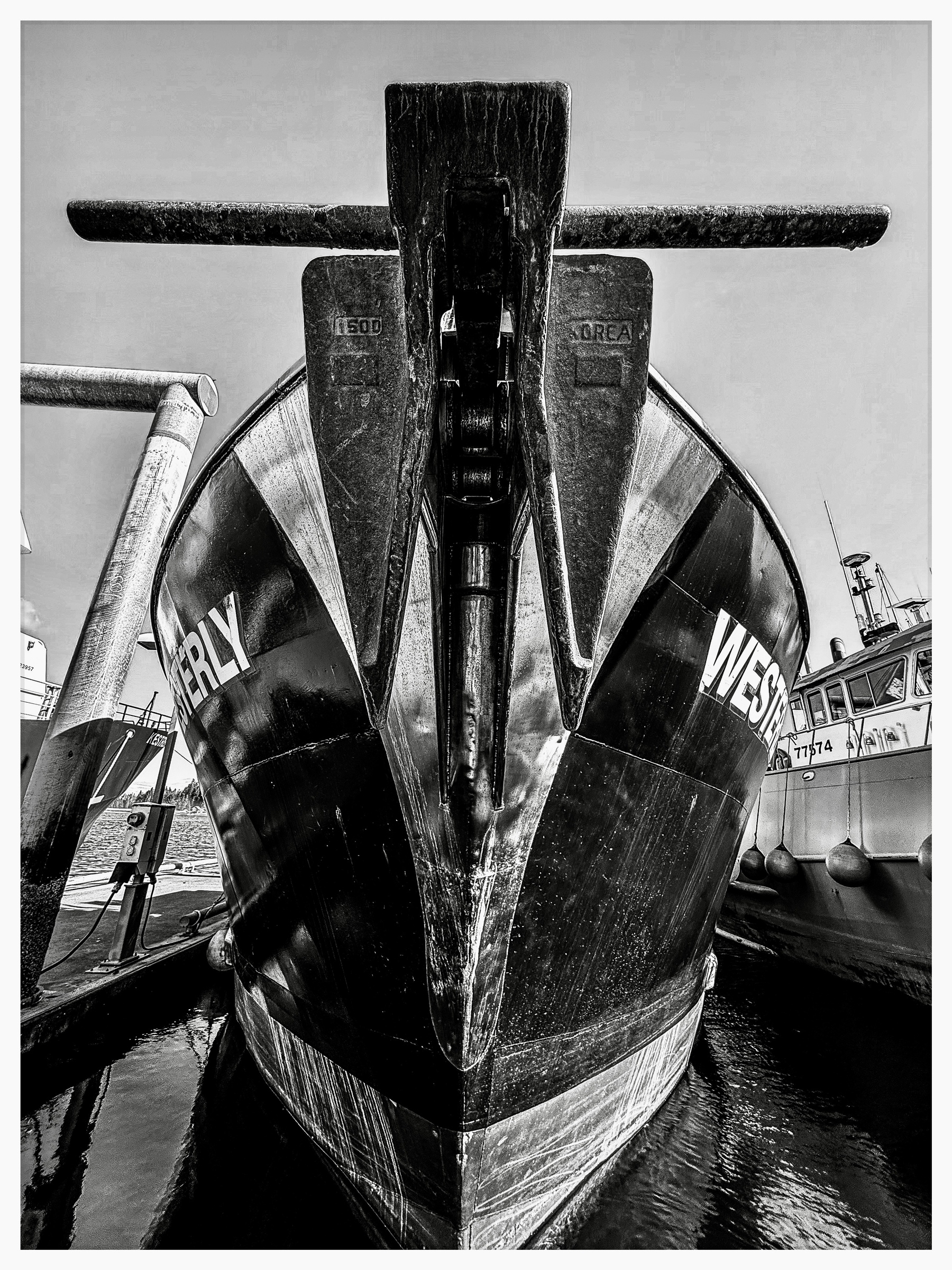 Auto-generated description: A black and white photograph captures the imposing front view of a large ship docked alongside other boats.