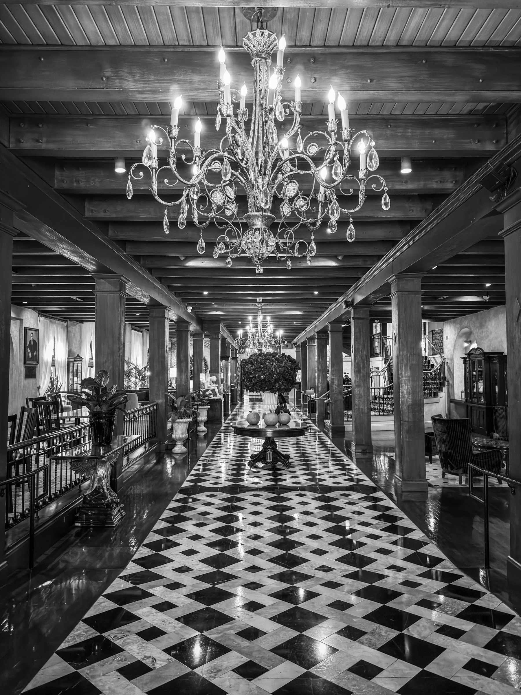 Auto-generated description: A grand hallway features a large chandelier, a checkered floor, and ornate furnishings.