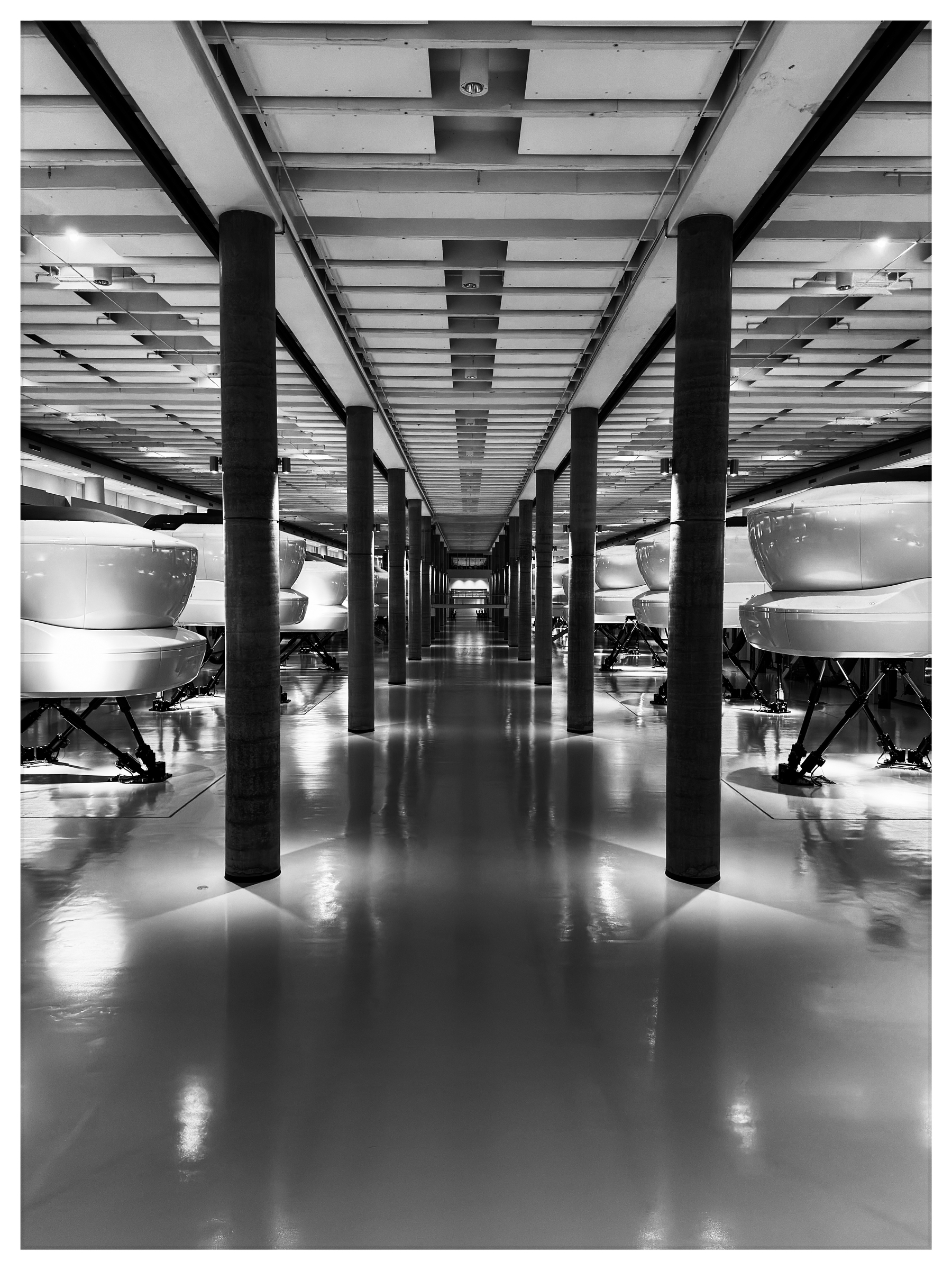 Auto-generated description: A sleek, futuristic corridor features flight simulators lined up on either side with a polished reflective floor.