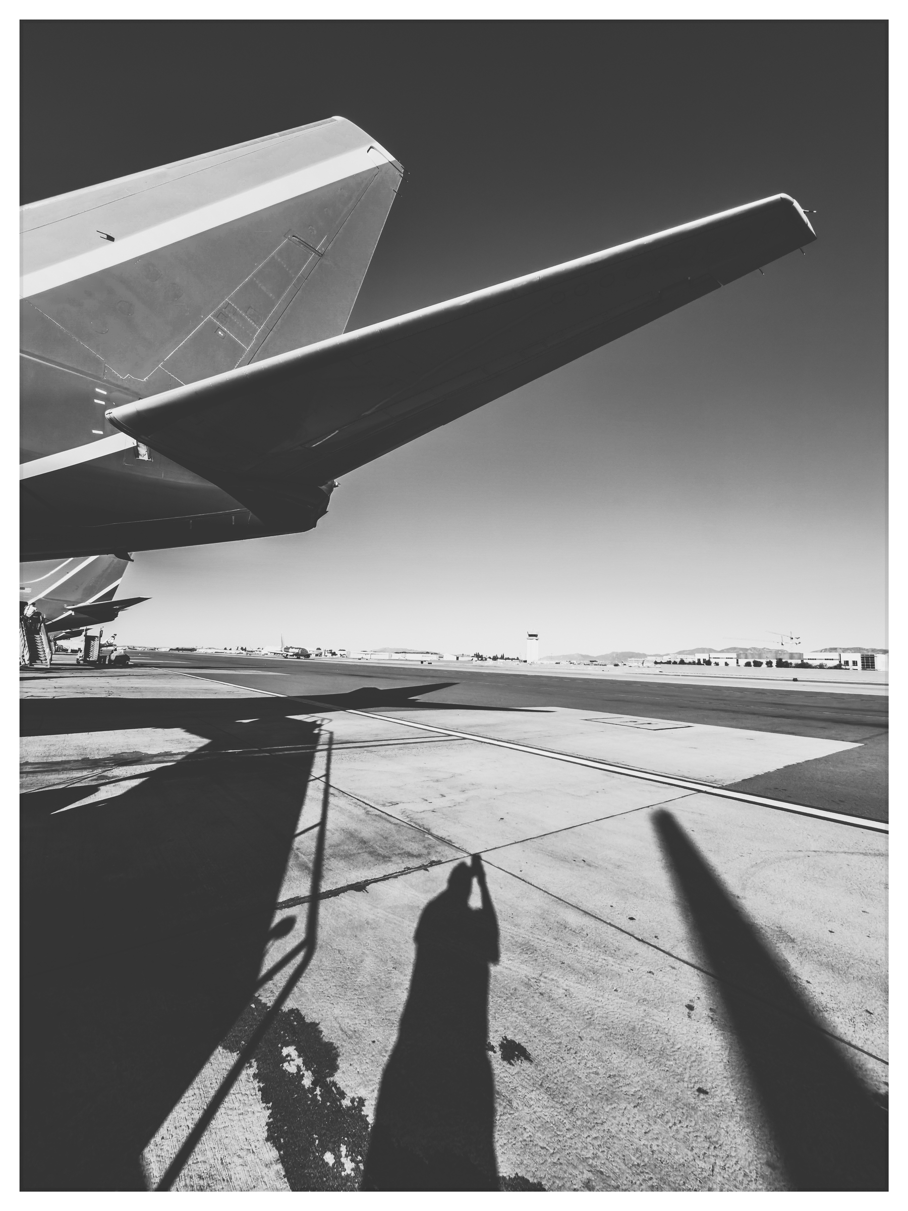 Auto-generated description: An airplane's tail and wing are captured from beneath on an airfield, casting a shadowy silhouette against the tarmac.