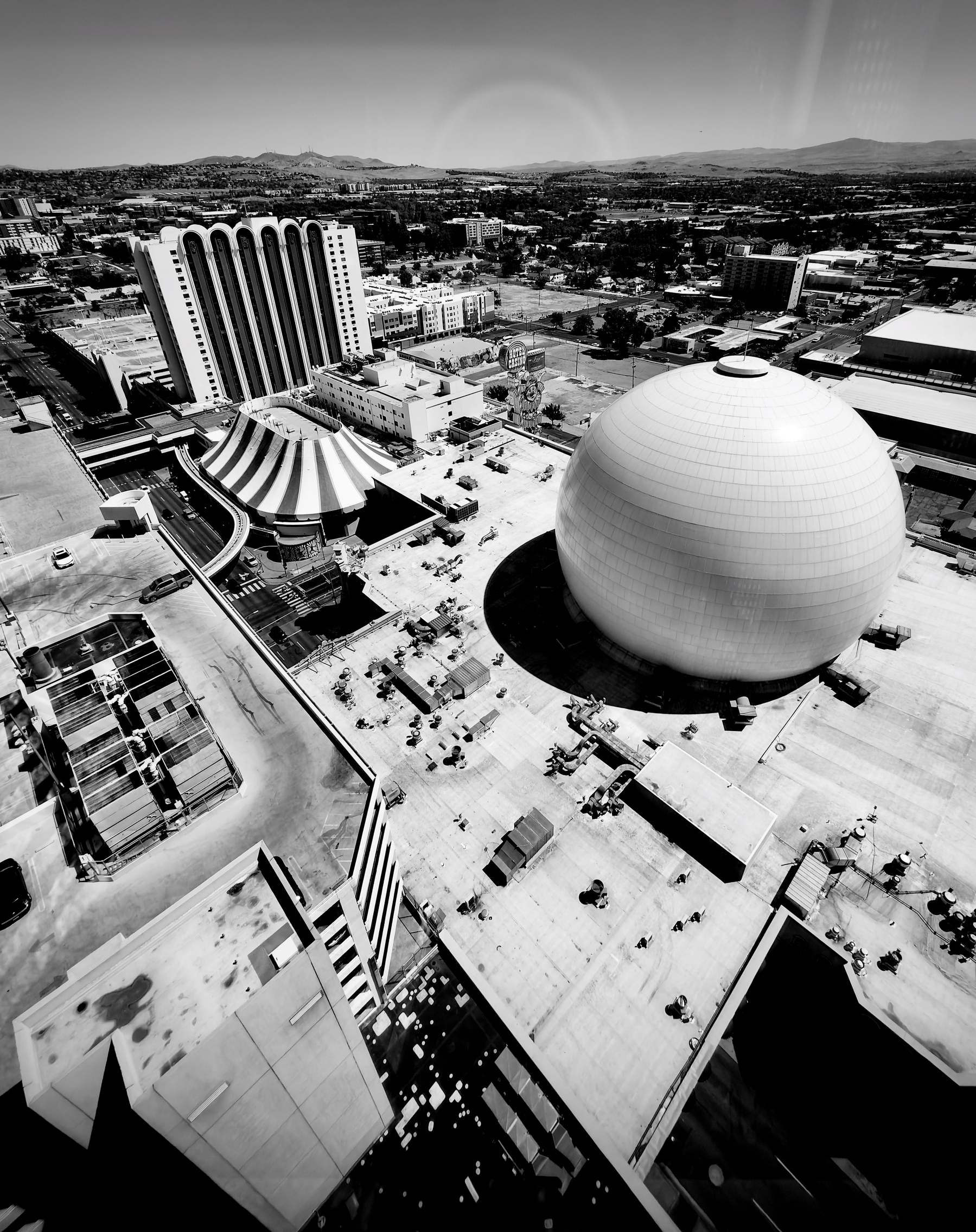 Auto-generated description: A large spherical building is situated among other structures in an urban area with mountains visible in the background.
