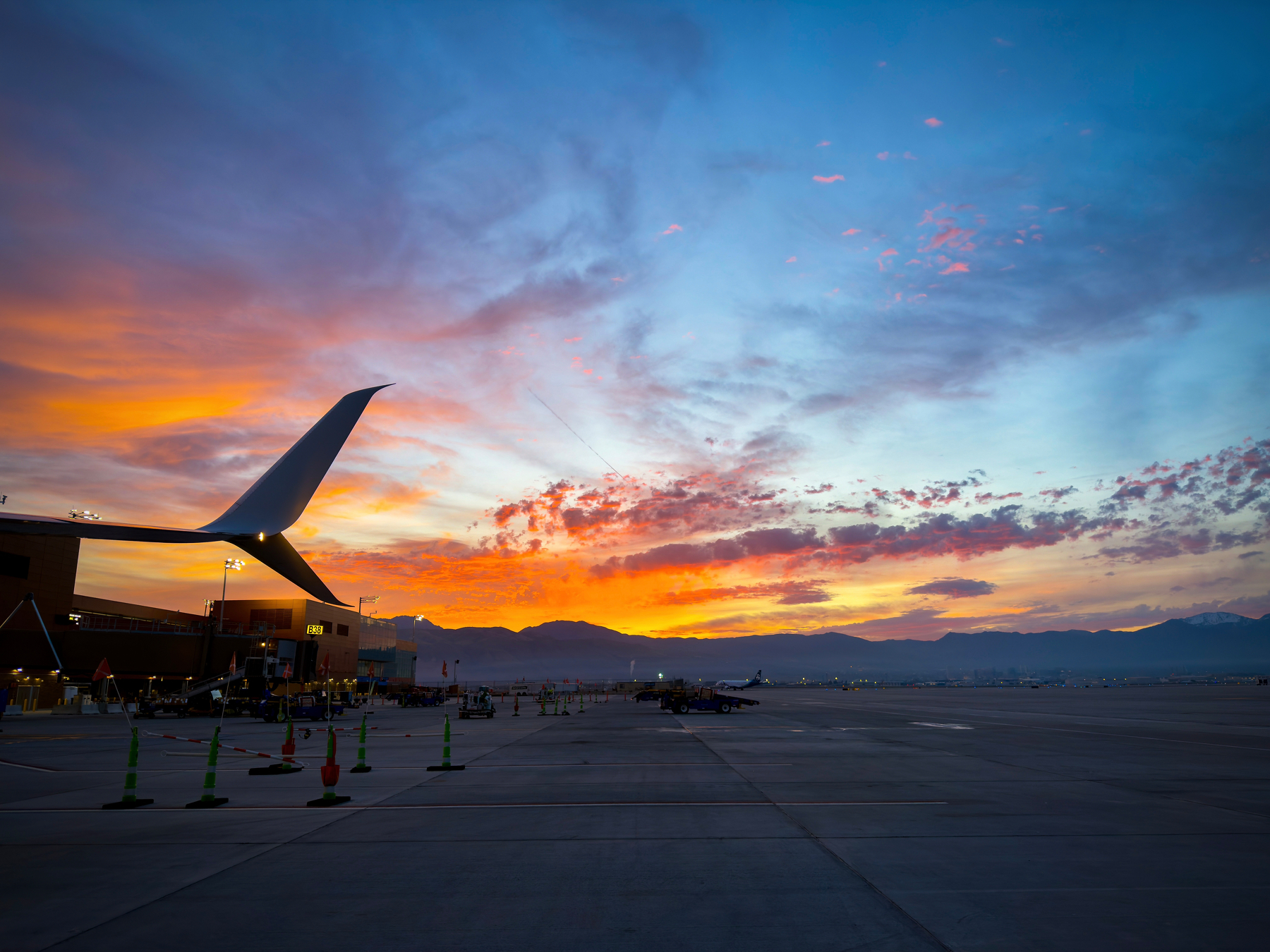 A vibrant sunset with dramatic clouds is visible over an airport tarmac with a plane's wing in the foreground.