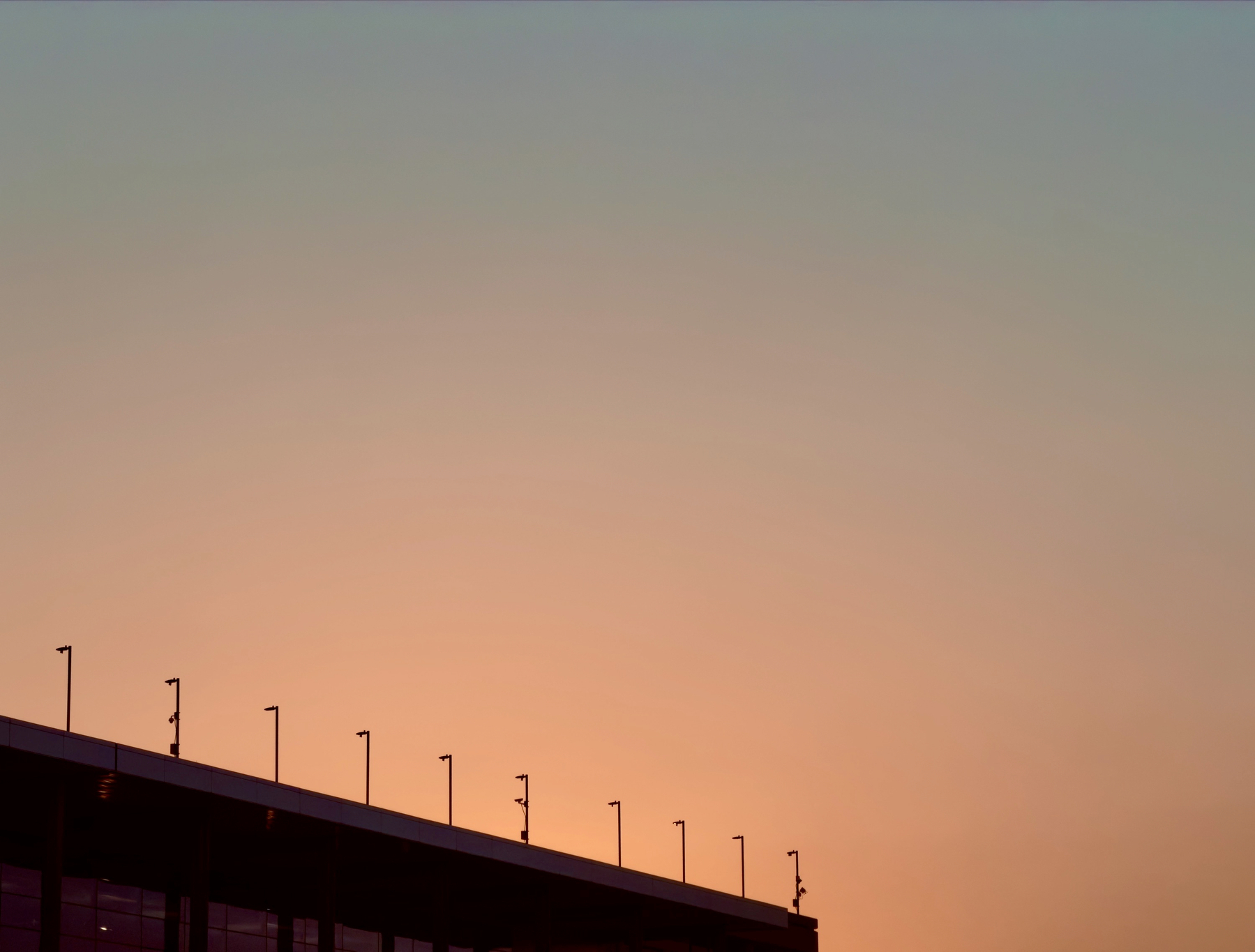 Auto-generated description: A building roof is silhouetted against a clear sky at sunset with a gradient of warm colors.