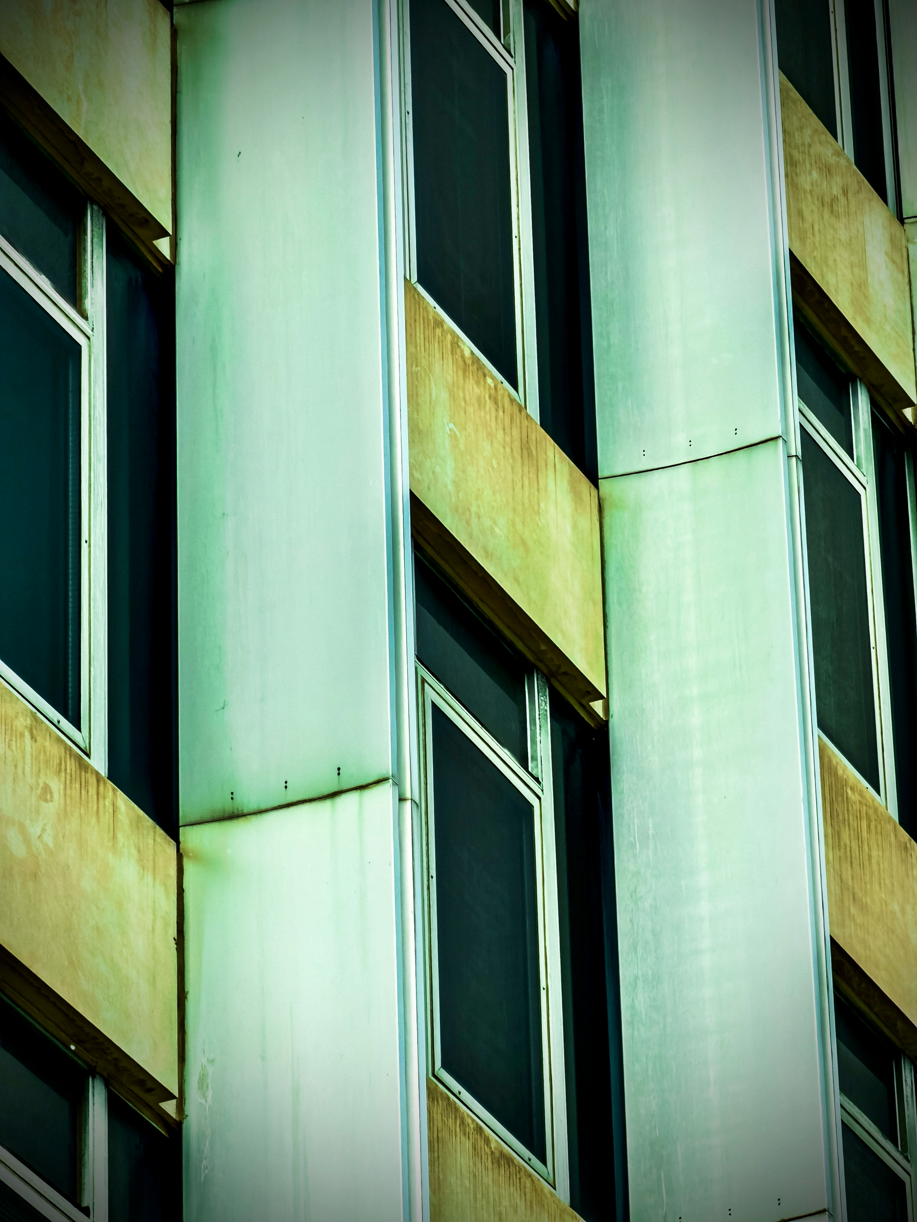 Auto-generated description: A building facade featuring a series of large rectangular windows framed by vertical metal panels with discoloration and weathering.