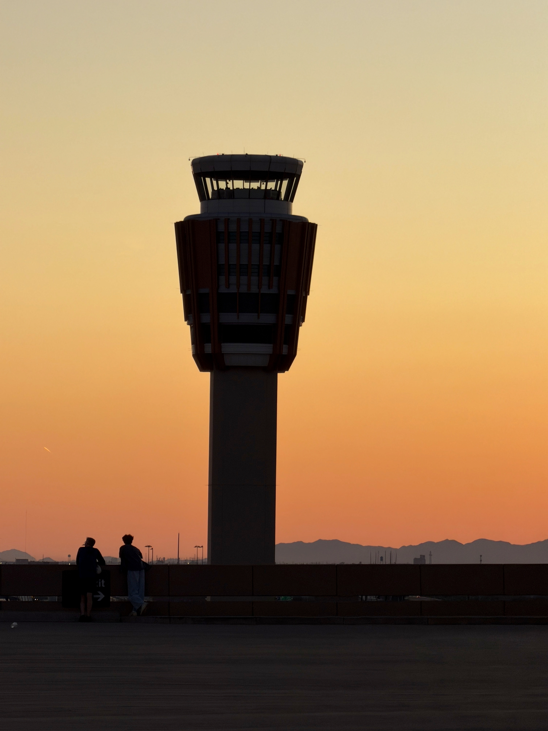 Auto-generated description: A silhouette of an airport control tower is set against a warm, orange sunset sky.